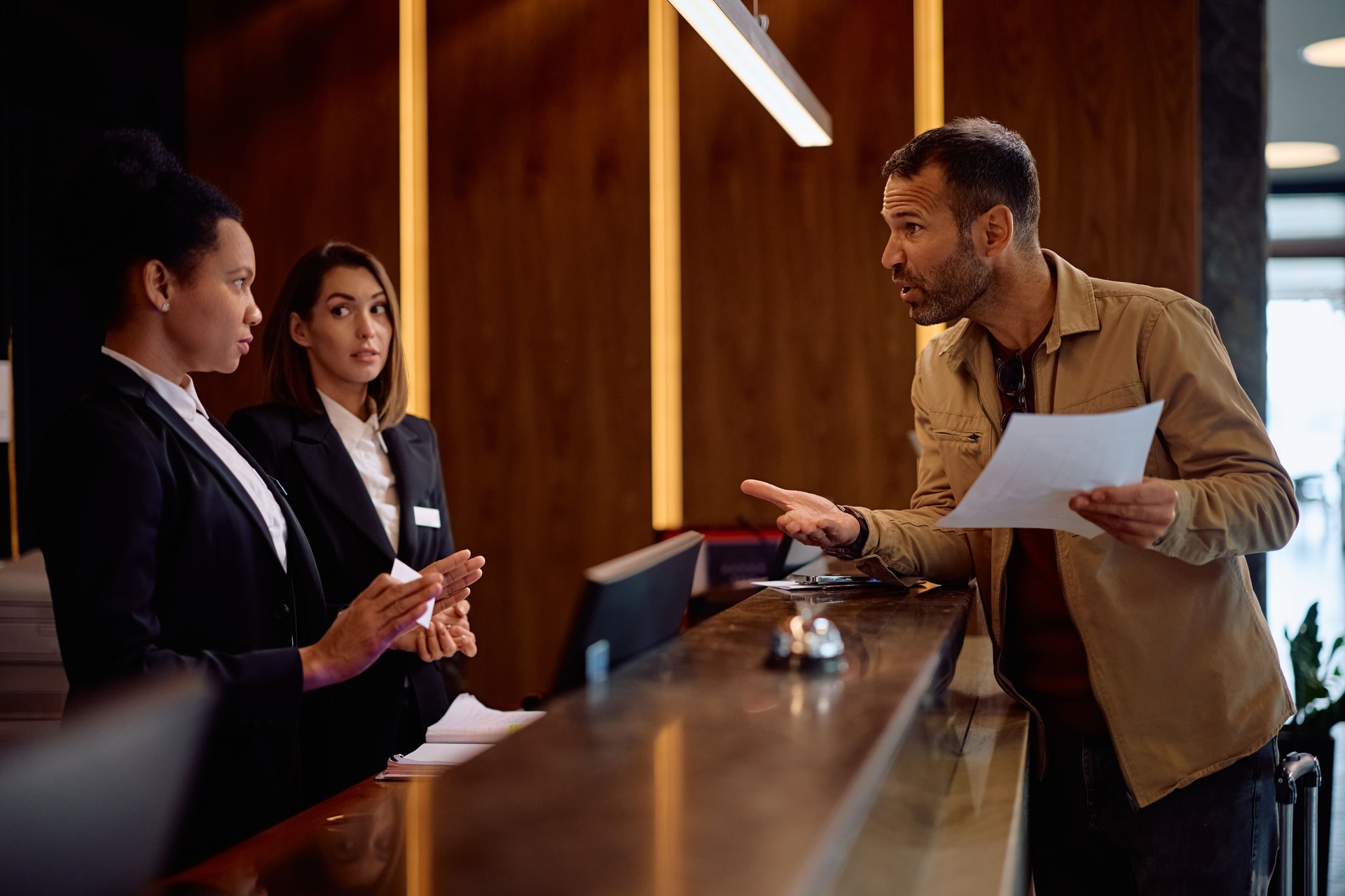 Dissatisfied hotel guest having arguing with receptionists at front desk.